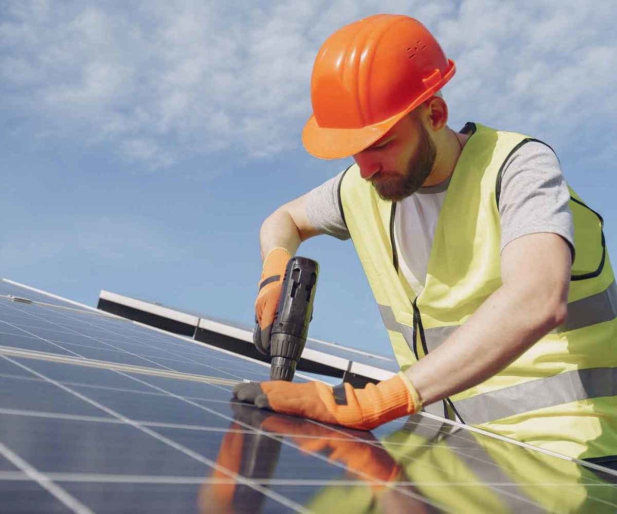 Installatör monterar solcellspanel med borrmaskin under klar himmel