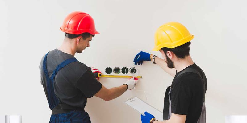 Två elektriker installerar eluttag i en vägg