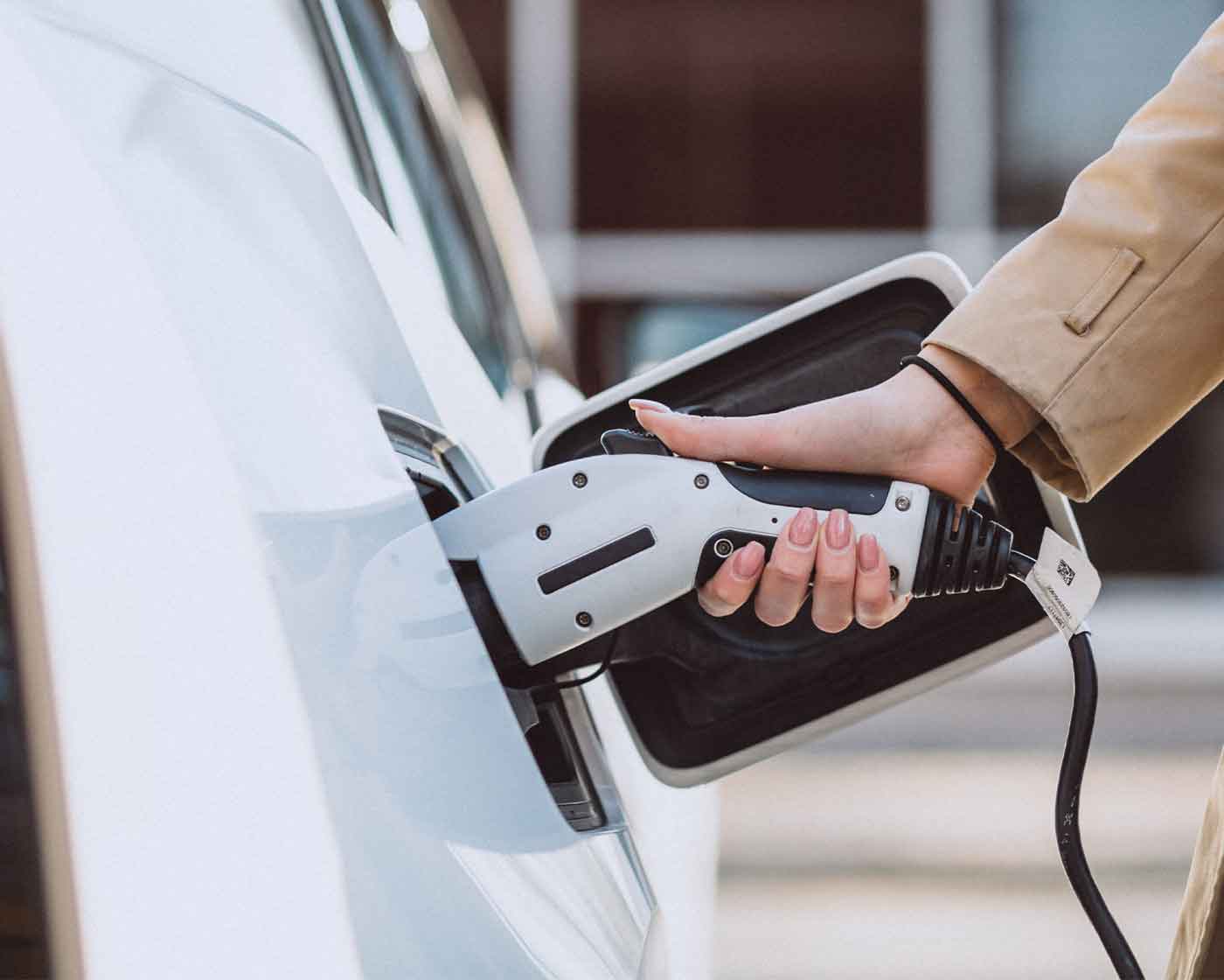 Kvinna ansluter laddkabel till elbil vid laddstation i Borås